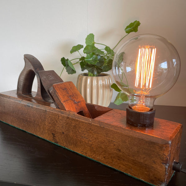Vintage lamp crafted by shades at grays from an antique carpenters' plane, with edison bulb, lit, side view.
