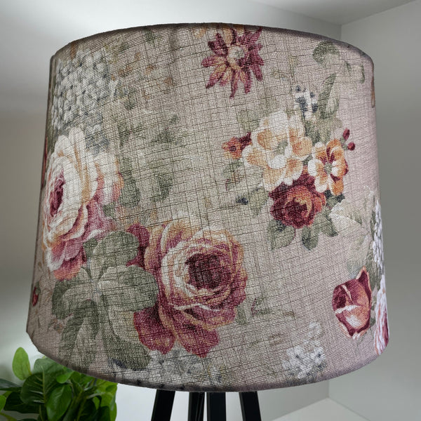 Vintage style floral pattern of reds and cream blooms on blush pink background, lit lampshade by shades at grays.