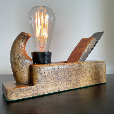 Vintage table lamp crafted by shades at grays from original old carpenters plane with edison bulb, lit, front view.