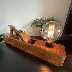 Vintage table lamp handcrafted from authentic carpenters plane by shades at grays, with addition of edison bulb, front view.