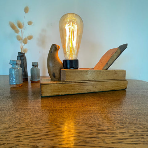 Vintage wood plane lamp with edison bulb, lit, upcycled by shades at grays, long front view.