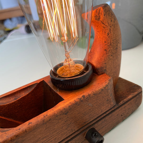 Warm glow of edison bulb on wooden table lamp, handcrafted from vintage carpenter's wood plane.