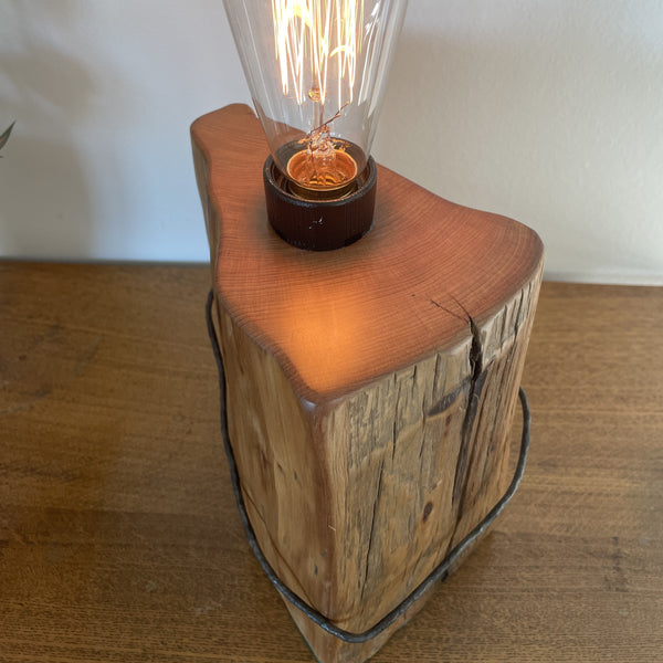 Wood table lamp crafted from vintage tōtara fence post with original wire and replica edison bulb, lit, front and top view, handcrafted by shades at grays.