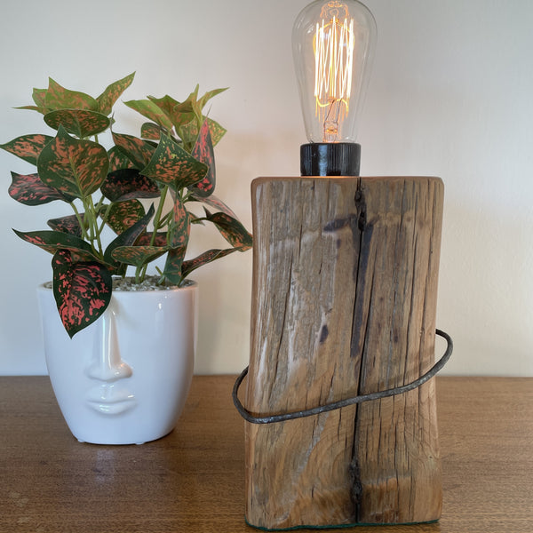 Wood table lamp crafted from vintage tōtara fence post with original wire and replica edison bulb, lit, front view, handcrafted by shades at grays.