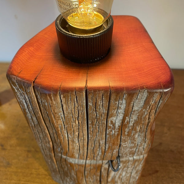 Wood table lamp handcrafted by shades at grays from tōtara fence post, with original staple and edison bulb, lit, top view.