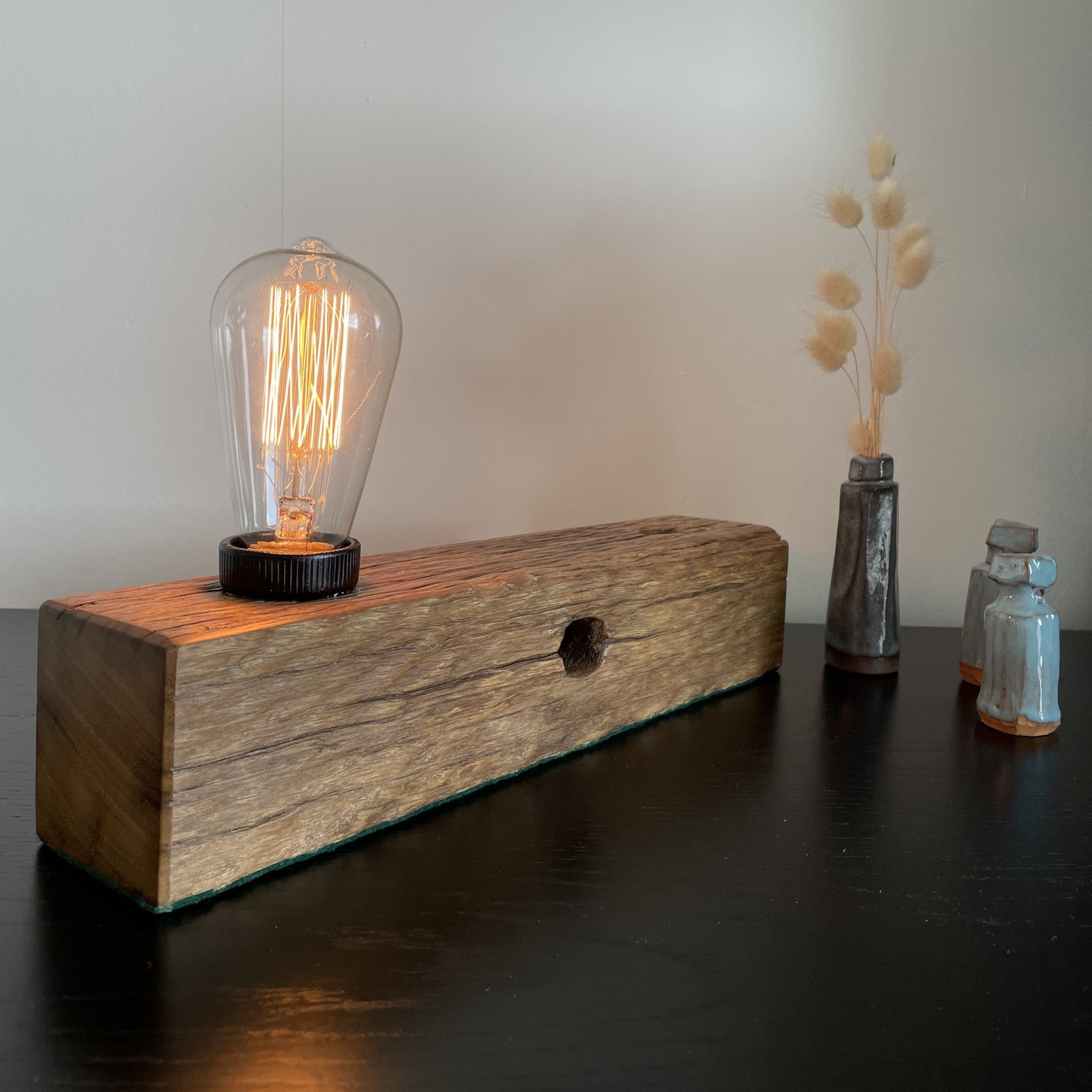 Wooden table lamp upcycled from old telegraph pole with edison bulb, lit.