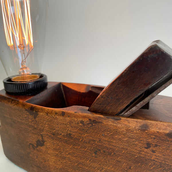 Wooden table lamp, handcrafted from vintage carpenter's plane, dark honey wood and edison bulb, lit, close up of side.