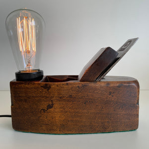 Wooden table lamp, handcrafted from vintage carpenter's plane, dark honey wood and edison bulb, lit.