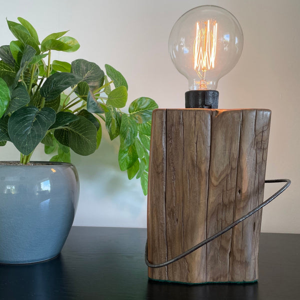 Rustic tōtara fence post crafted into a wood table lamp with replica edison bulb by shades at grays, fron view  lit.