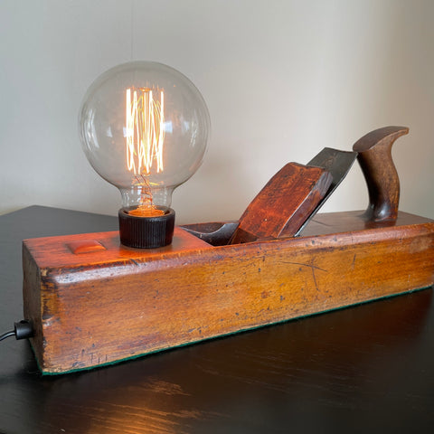 Vintage carpenter's wood plane table lamp crafted by shades at grays, front view, lit.