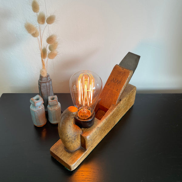 Vintage table lamp crafted by shades at grays from original old carpenters plane with edison bulb, lit, top view.