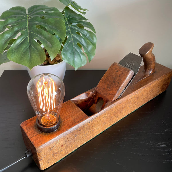 Wooden table lamp crafted from vintage carpenter's plane, cleaned and polished with natural beeswax with replica edison bulb, lit.