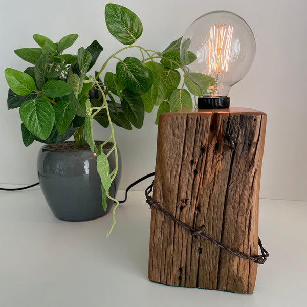 Wooden table lamp handcraafted from totara post with original fence wire, front view, lit.