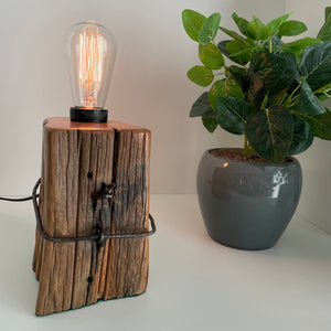 Wooden table lamp handcrafted from vintage totara post with original wire and replica edison bulb, lit.