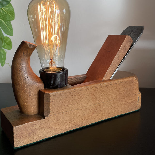 Original vintage wood plane lamp with edision bulb, lit, by shades at grays, close up of smooth front and 'rhino horn.'