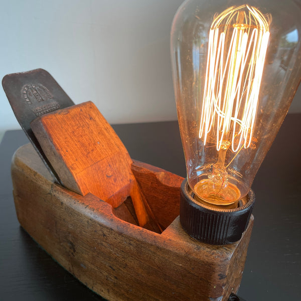 Wood lamp created by shades at grays from vintage wood plane, with branded cutting blade and reflection in honey coloured woo,, lit.