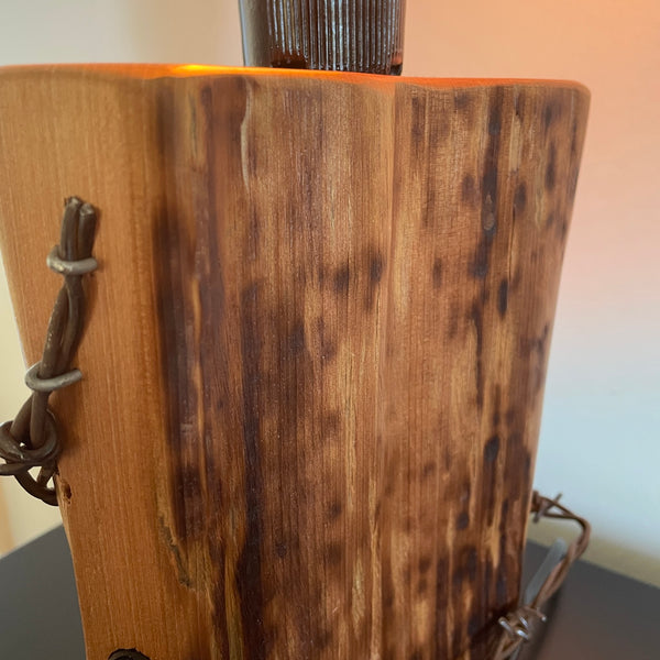 Wood table lamp crafted from reclaimed tōtara post with authentic barbed wire and the adition of an edision bulb, close up of side view, by shades at grays.