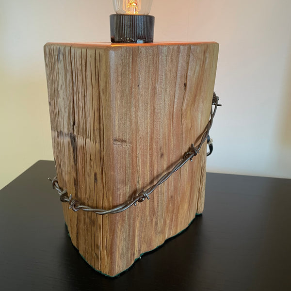 Wood table lamp crafted from reclaimed tōtara post with authentic barbed wire and the adition of an edision bulb, front and side view by shades at grays.