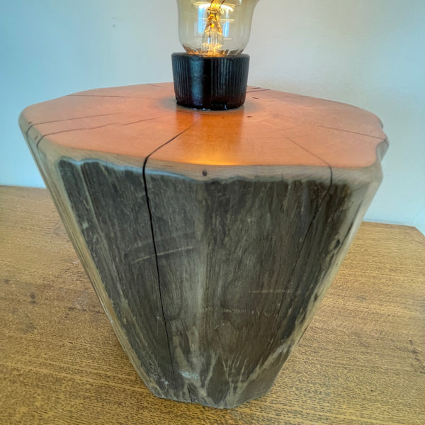 Wood table lamp handcrafted by shades at grays from authentic tōtara post, close up of exposed, polished wood grain and lit bulb.