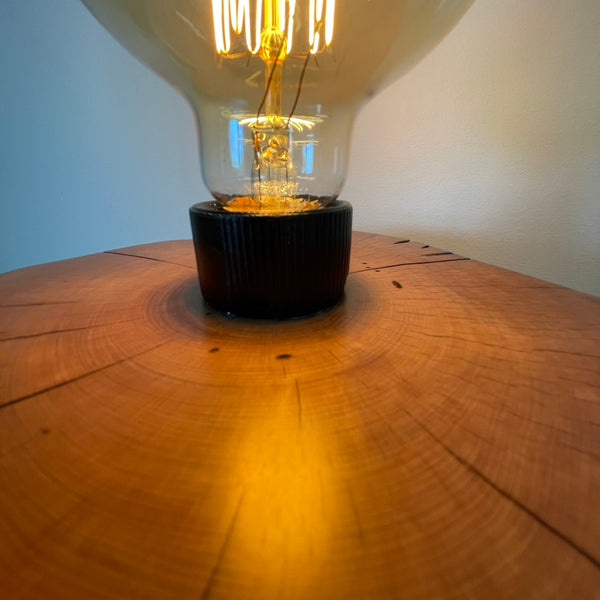 Wood table lamp handcrafted by shades at grays from authentic tōtara post,  smooth polished wood grain of top and light reflection, close up.