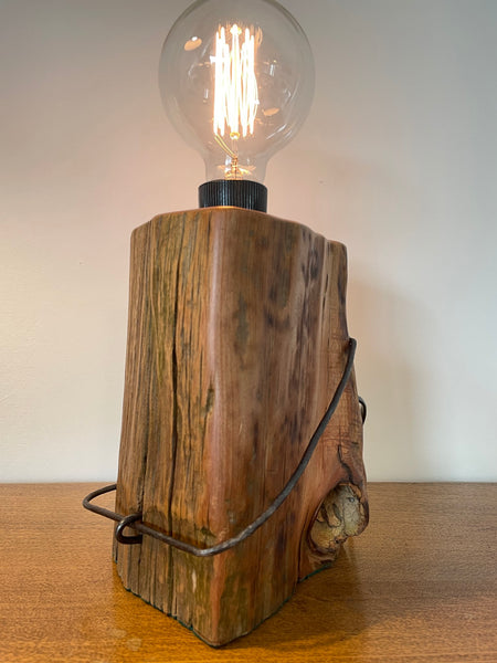 Wood table lamp handcrafted by shades at grays from vintage tōtara post with original wire and iron clip, smooth polished sides and replica edison bulb, lit.