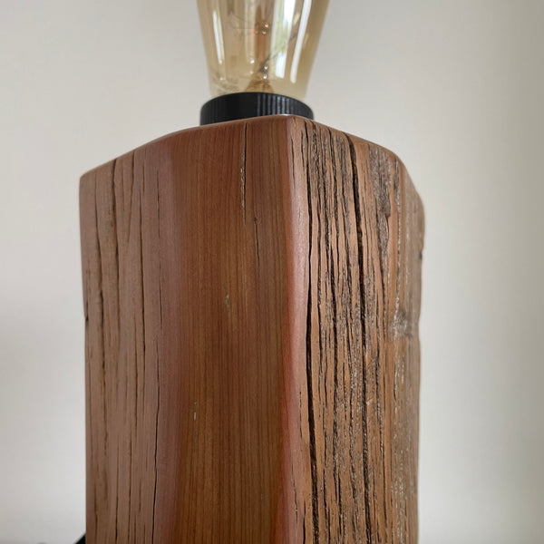 Wooden lamp with, polished exposed wood grain and a visible bulb on a plain background