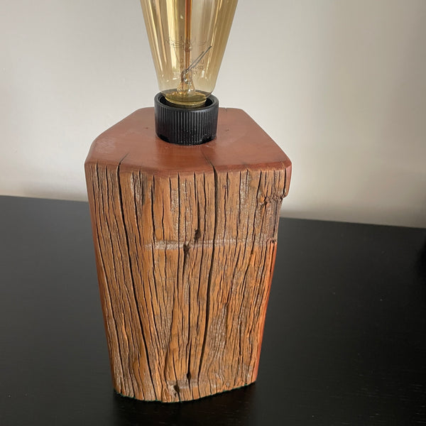 Wooden lamp with a textured base and visible replica edison bulb, unlit, on a dark surface.