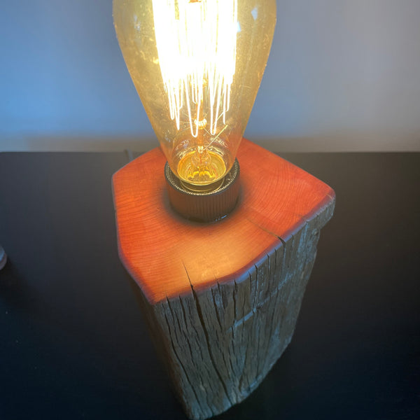 Vintage-style light bulb on a wood table lamp base against a dark background