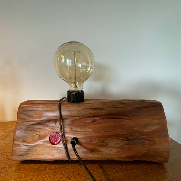 Wood table lamp reclaimed from vintage tōtara post with retained wire, back view with makers red branding mark and black lead.
