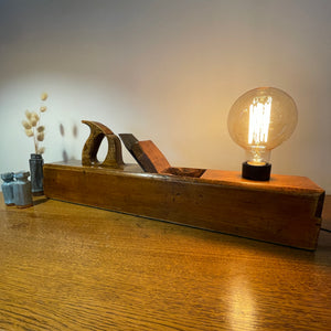 Wood table lamp upcycled from large carpenter's plane with replica edison bulb, lit, front view.