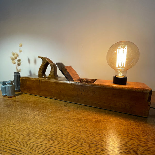 Wood table lamp upcycled from large carpenter's plane with replica edison bulb, lit, front view.