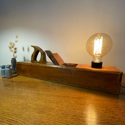 Wood table lamp upcycled from large carpenter's plane with replica edison bulb, lit, front view.