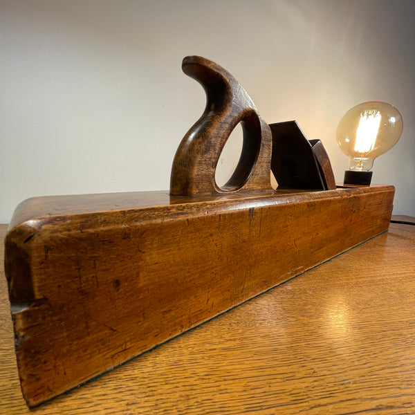 Wood table lamp upcycled from large carpenter's plane with replica edison bulb, lit, side and back view.