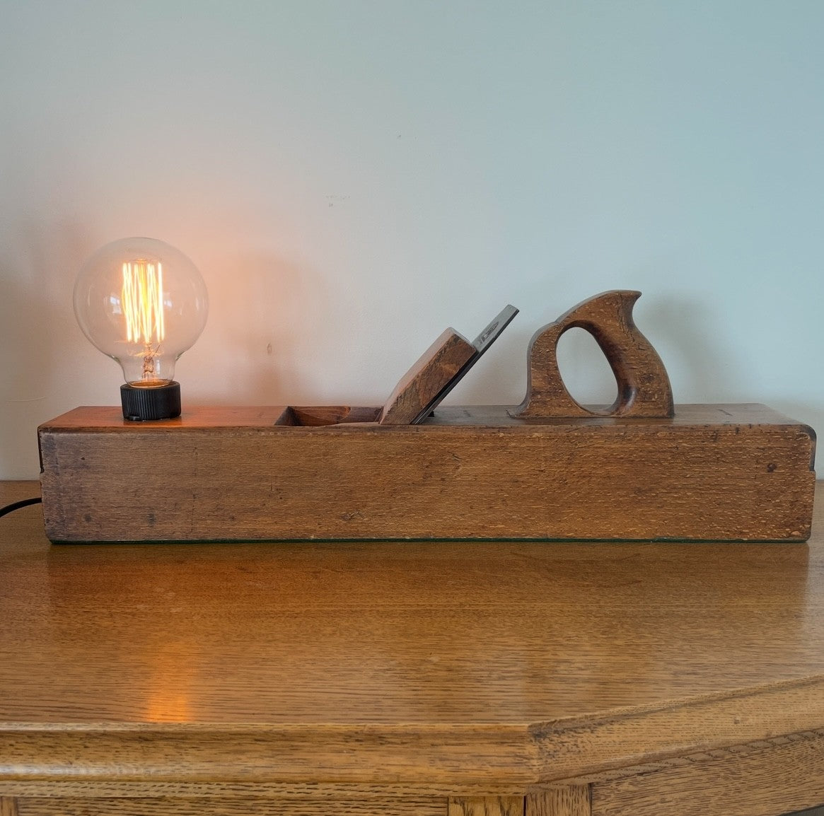 Wood table lamp upcycled from large vintage carpenters plane, front view with replica edison bulb, lit, by shades at grays