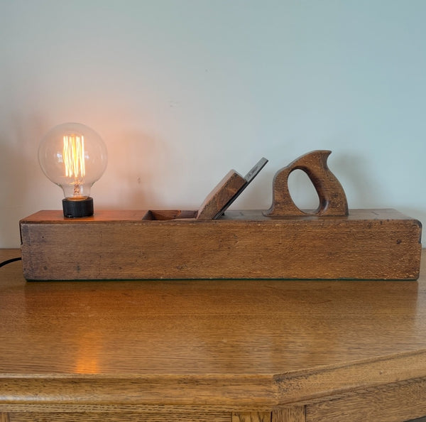 Wood table lamp upcycled from large vintage carpenters plane, front view with replica edison bulb, lit, by shades at grays
