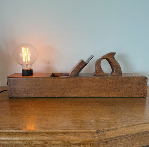 Wood table lamp upcycled from large vintage carpenters plane, front view with replica edison bulb, lit, by shades at grays