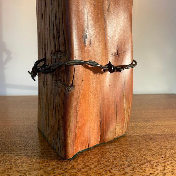 Wood table lamp with polished grain, original wire and replica edison light bulb, lit, close up of smooth side and wire by shades at grays.