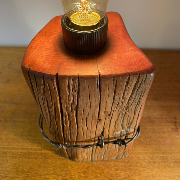 Wood table lamp with polished grain, original wire and replica edison light bulb, lit, smooth top grain, by shades at grays.