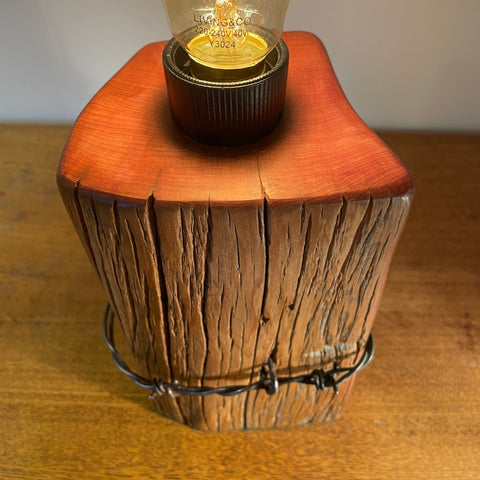 Wood table lamp with polished grain, original wire and replica edison light bulb, lit, smooth top grain, by shades at grays.