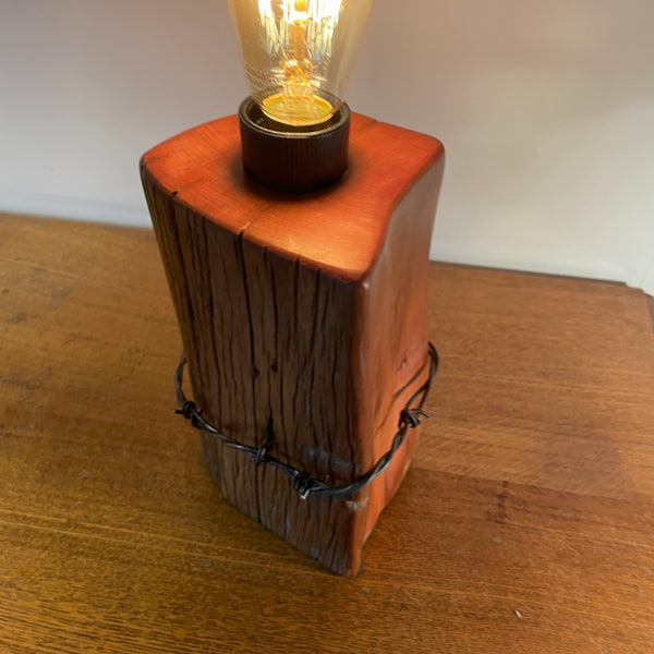 Wood table lamp with polished grain, original wire and replica edison light bulb, lit, top and side views by shades at grays.