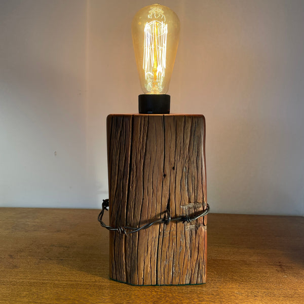 Wooden lamp with a lit bulb on a wooden surface