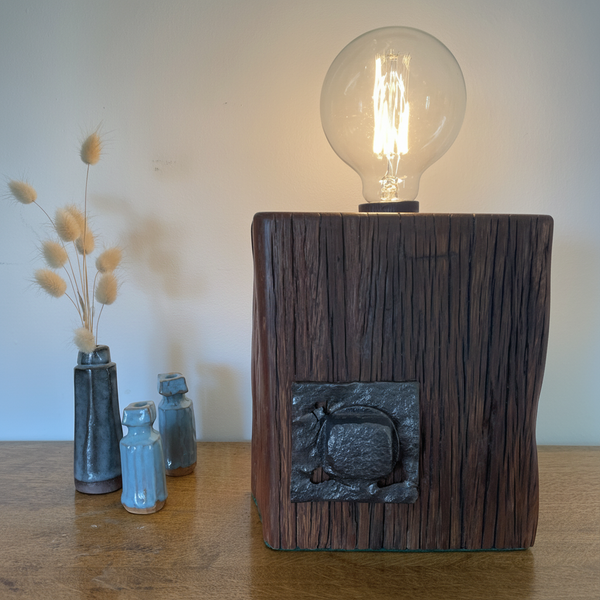Wood table lamp handcrafted by shades at grays from wharf timber with original bolt and replica edison bulb, lit, front view.