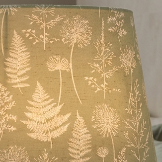 Lit tapered lampshade in Meadow Green fabric on a ceramic base beside a bed.