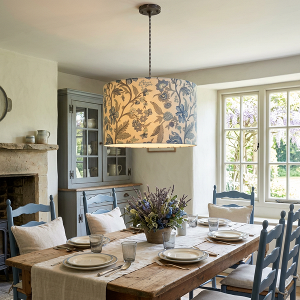 Drum ceiling pendant in French General Parterre Pearl French Blue fabric glowing above a wooden dining table.