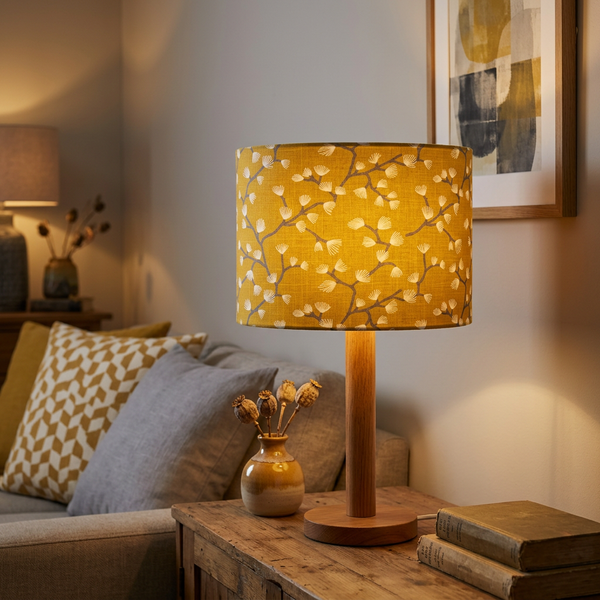 Lit drum lampshade in Spring Buds Sunflower fabric on a timber table lamp base in a cosy living room.