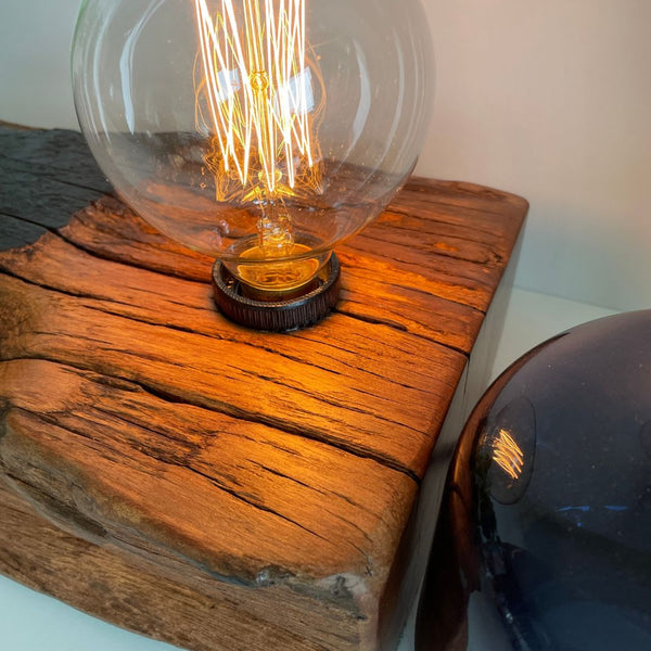 Beeswax polished wood grains and edison light bulb reflecting in blue ornament.