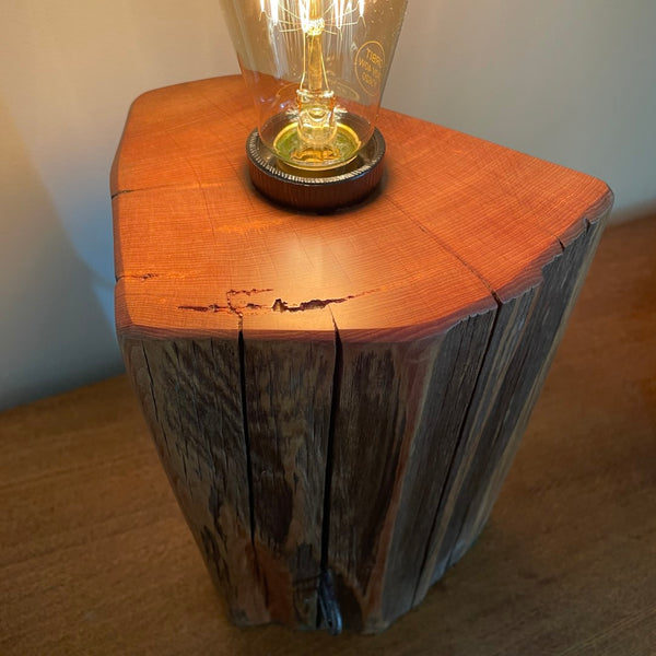 Bees wax polished top with glow of edison light bulb on unique wooden table lamp, handcrafted from old totara post.