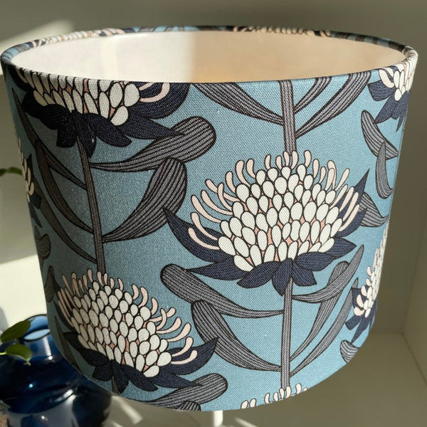 Blue and white waratahs fabric on medium drum light shade, close up.