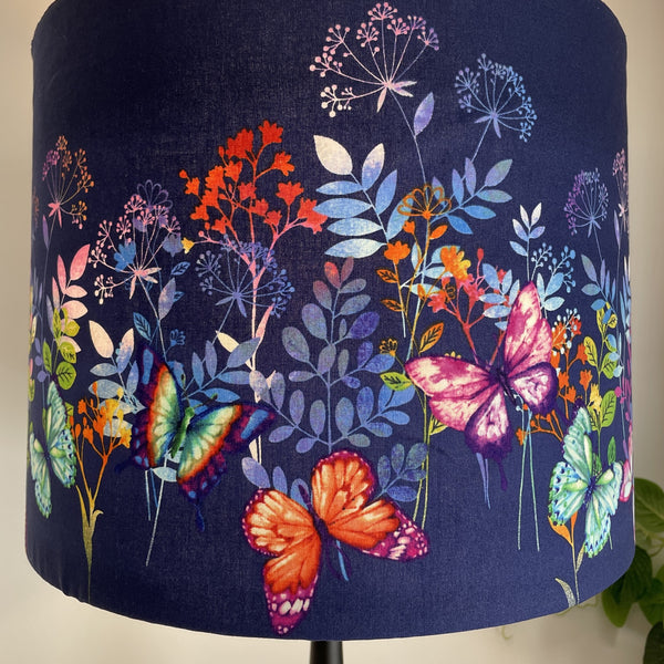 Dark indigo background with multi colour butterflies and foliage on large drum lamp shade, bottom half.