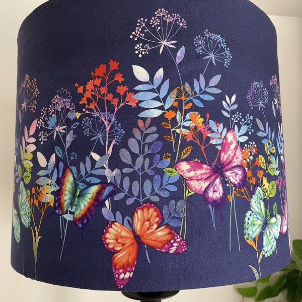 Dark indigo background with multi colour butterflies and foliage on large drum lamp shade, unlit.